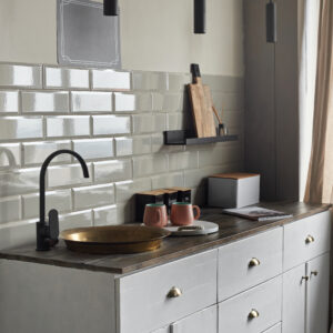 Modern creative idea of small kitchen with gray tiles wall with old fashion copper sink and modern faucet, tea and coffee containers, pink cups, and magazine on wooden counter.